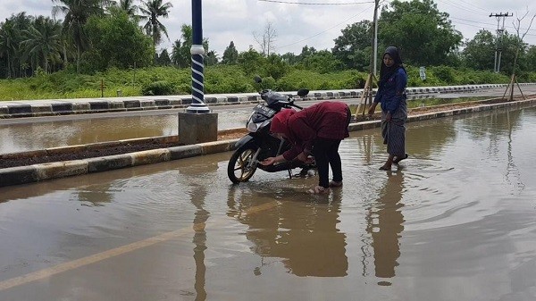 Dua orang warga sedang mencuci sepeda motor di genangan air Jalan Pramuka
